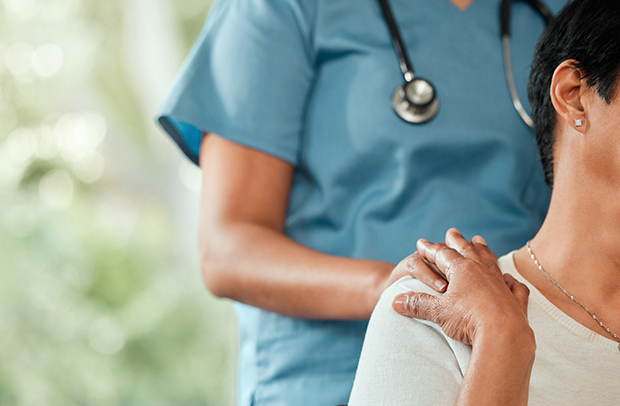 A nurse in blue scrubs with a patient in a white shirt.