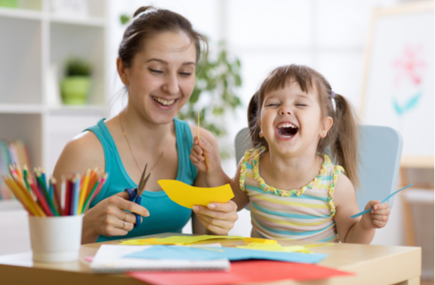 Close-up of a mother and her young daughter sitting at a table and laughing while doing arts and crafts